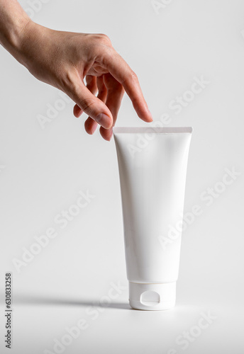 Hand, finger touching large cream tube, cosmetic beauty product mockup, blank package for moisturizer mask