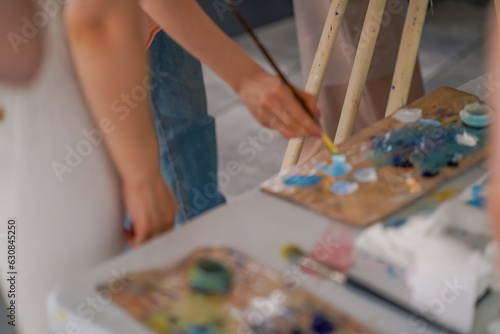A close-up of a girl artist sitting near an easel and taking paint from a palette with a brush the concept of love of fine art 