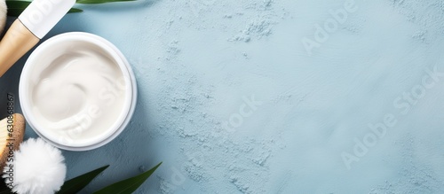 a flat lay of skin care products including a face massage brush, hyaluronic acid, cream for the face, and a clay mask. The background is blue and empty space for text or copy. It represents skin