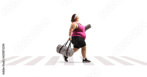 Overweight young woman in sportswear carrying a bag and walking at a pedestrian crosswalk