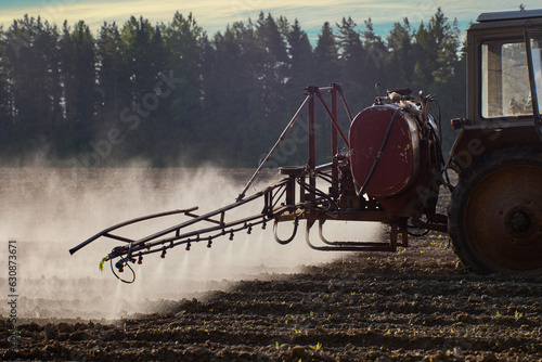 Spraying crops with chemicals such as pesticides or herbicides using sprayer mounted on wheeled tractor. photo