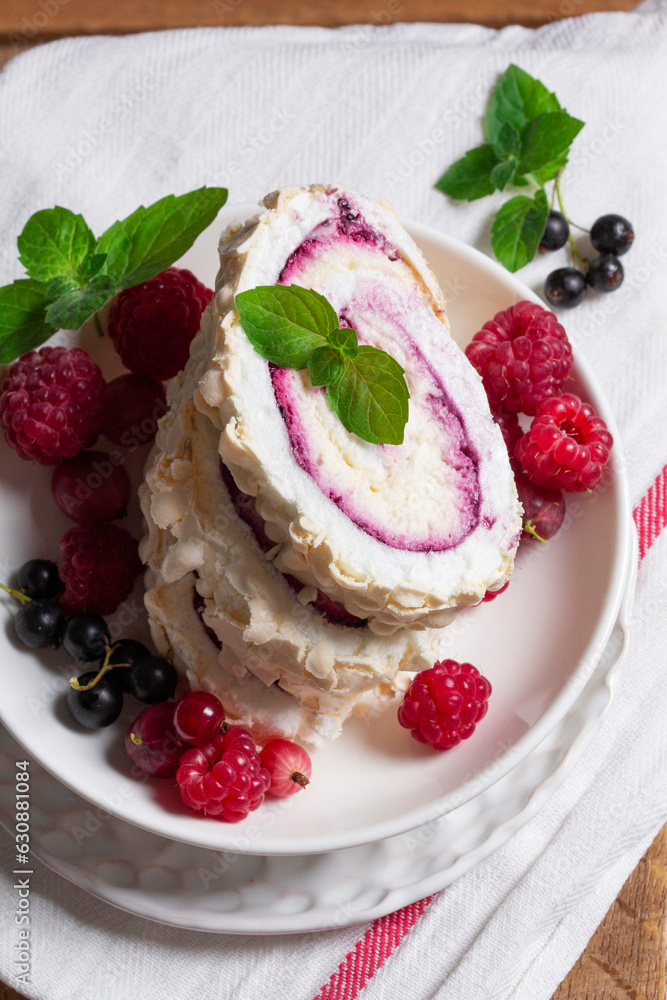 Meringue roll with whipped cream and currant curd, served with berries on a ceramic plate. Rustic style.