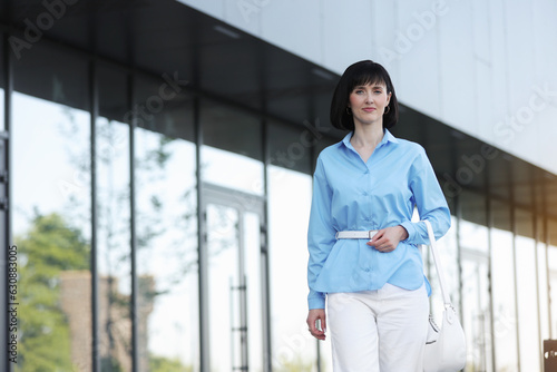 Relaxing and confident young business woman or entrepreneur walks by the modern office building company outdoors. Successful female career. Business people lifestyle  copy space.