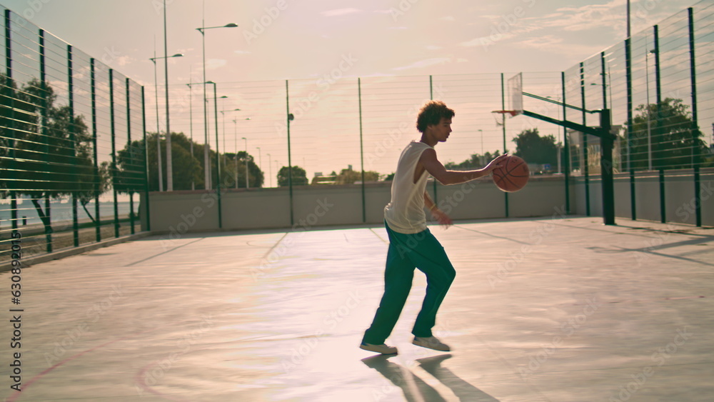 Involved teenager bounce ball at stadium. Basketball player making basket throw