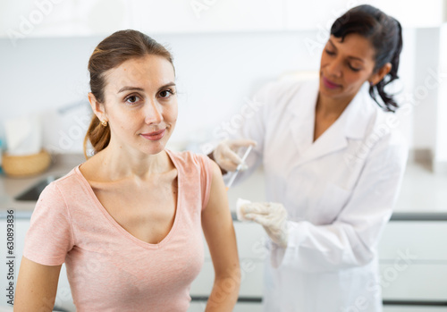Portrait of smiling young adult woman getting injection during visit at doctors office