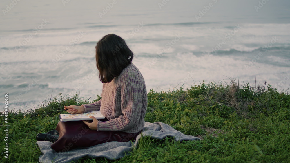 Lonely brunette sitting blanket with book looking gloomy seascape. Romantic girl