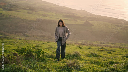 Attractive girl climbing hill covered green grass. Woman walking near calm ocean © stockbusters