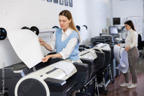 Woman using printer while working in print shop. Female printshop worker using printing device.