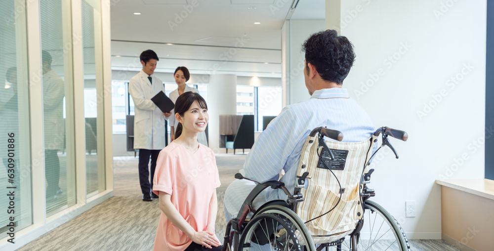 病院で車椅子に乗った患者と会話をする看護師 病院で車椅子に乗った患者と会話をする看護師