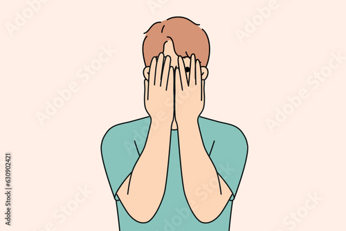 Man closes eyes with hands and peeps, feeling excited in anticipation of surprise or panic after receiving threats. Guy feels insecure and panic, trying to hide from problems that have arisen.