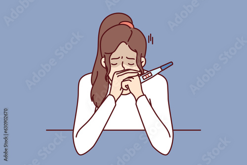 Frustrated pregnancy woman is crying holding pregnancy test with two strips and sitting at table. Concept pregnancy and need for family planning or problems associated with rejection of contraception