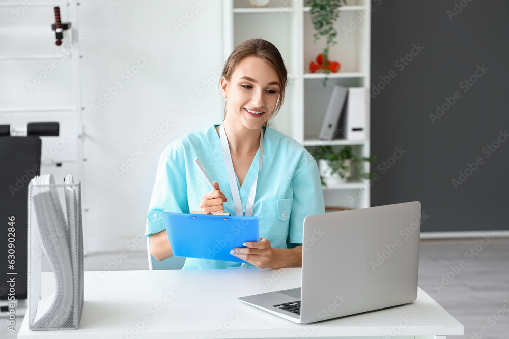 Female medical intern with clipboard using laptop at hospital Female medical intern with clipboard using laptop at hospital