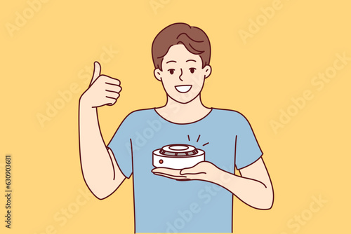 Man with smoke detector gives thumbs up recommending purchase of fire safety equipment. Young guy demonstrating quality smoke detector giving positive feedback after testing gadget