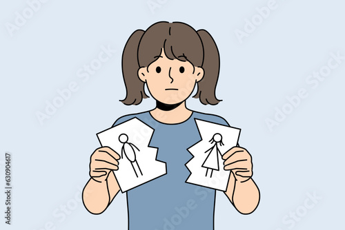 Sad little girl is nervous about parents divorce and is holding torn drawing of mom and dad. Sad child suffers after learning about dissolution of marriage between mother and father