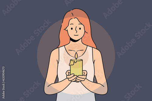 Woman with candle in hands looks at fire, performing religious ritual or seance. Positive girl holding candle to light way in dark due to power outage in house or broken lighting fixtures