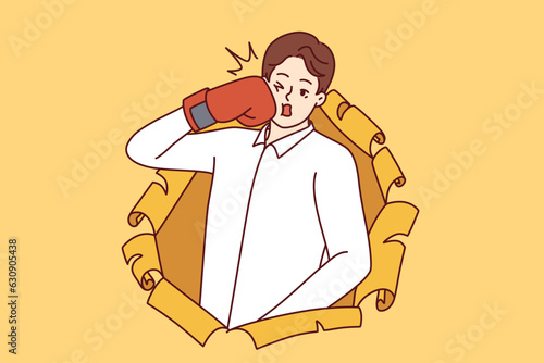 Man in boxing glove punches himself in face and peeking out of hole in torn paper. Young silly man boxer strikes, symbolizing actions that harm himself and cause problems in future.