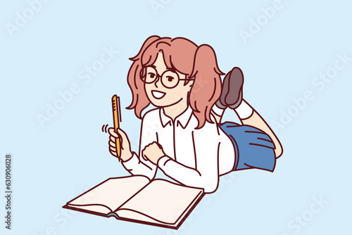 Little schoolgirl lies on floor with workbook and takes notes preparing for school lesson. Happy elementary school girl smiles and keeps personal diary with wishes or plans for holidays