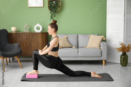 Fototapeta Naklejka Na Ścianę i Meble -  Sporty young woman practicing yoga with block at home