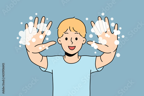 Little boy with foam shows soapy palms, recommending washing hands and following hygiene rules. Happy teenage boy doing preventive diseases and using soap after returning from school or walking