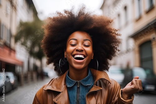 Jubilant young African American woman who, in a state of carefree abandon, throws up her hand with clenched fist, expressing her victorious spirit amidst the urban landscape..