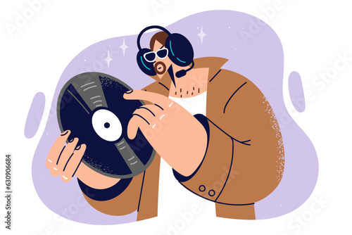 Man hipster holds vinyl record for phonograph, and listens to rare music on headphones.