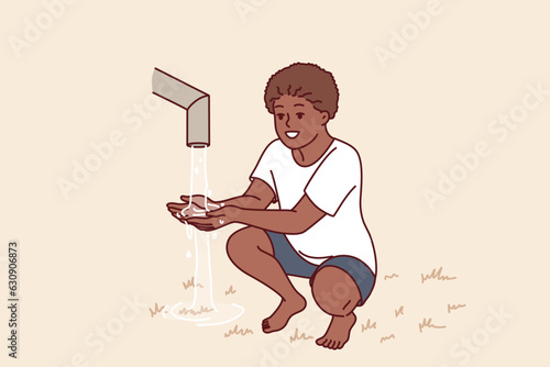 African boy sits near clean water faucet, rejoicing at opportunity to quench thirst during drought. Child drinks and draws water in palm of hand to drink, for concept acosania helping children Africa