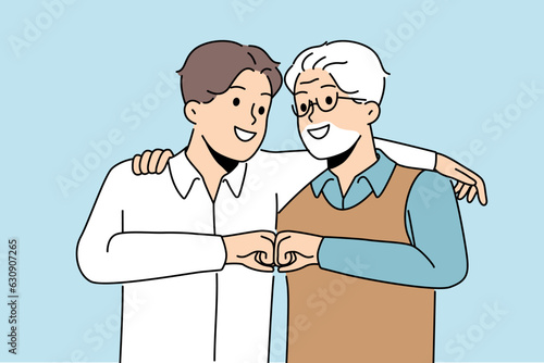Young son and elderly father hug and bump fists to demonstrate unity and friendship between generations. Man of different ages say together we are strength, calling to be friends for generations
