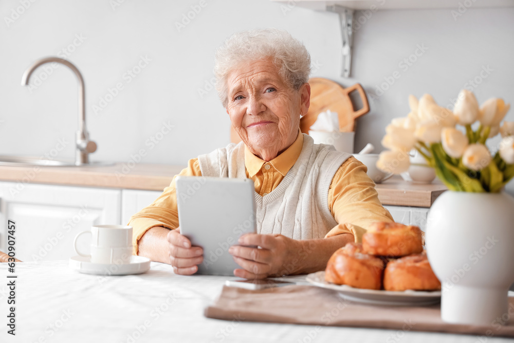 Senior woman using tablet computer at table in kitchen Senior woman using tablet computer at table in kitchen