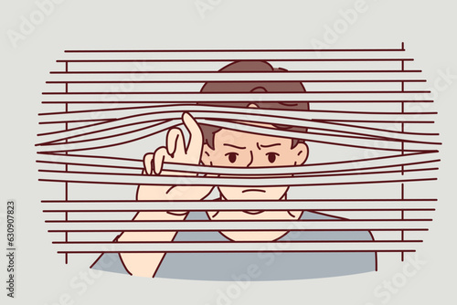 Man peeks through closed blinds to follow neighbor or find out secret information that is being hidden from him. Guy with suspicion and fear looks out window suffering from paranoia or schizophrenia