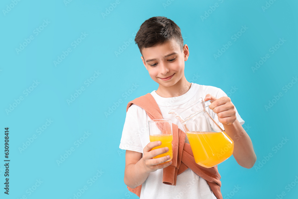 Little boy pouring orange juice into glass on blue background Little boy pouring orange juice into glass on blue background