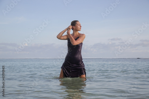 Creative portrait of female model in wet purple satin dress on the beach, stylish and elegant summer fashion