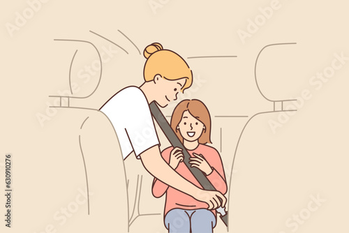 Caring mother uses child seatbelt to fasten little girl into passenger seat of car.