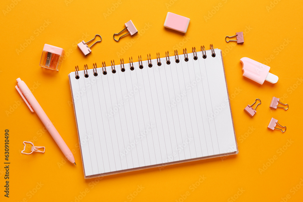 Notebook with different stationery supplies on orange background Notebook with different stationery supplies on orange background