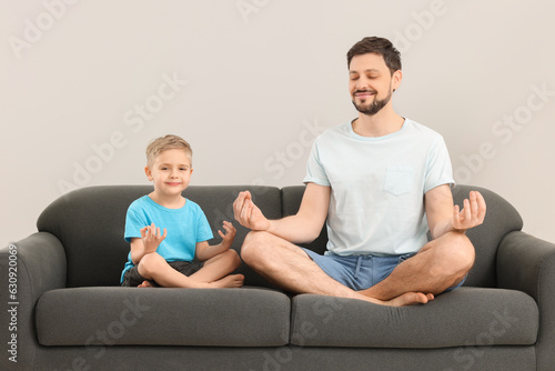 Father with son meditating together on sofa at home. Harmony and zen