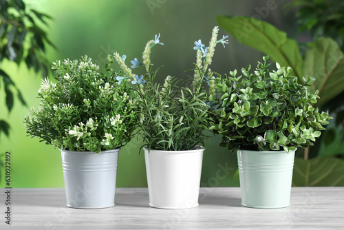 Different artificial potted herbs on white wooden table outdoors