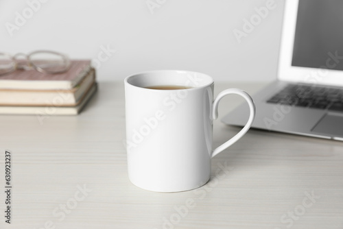 One ceramic mug with drink and laptop on white wooden table