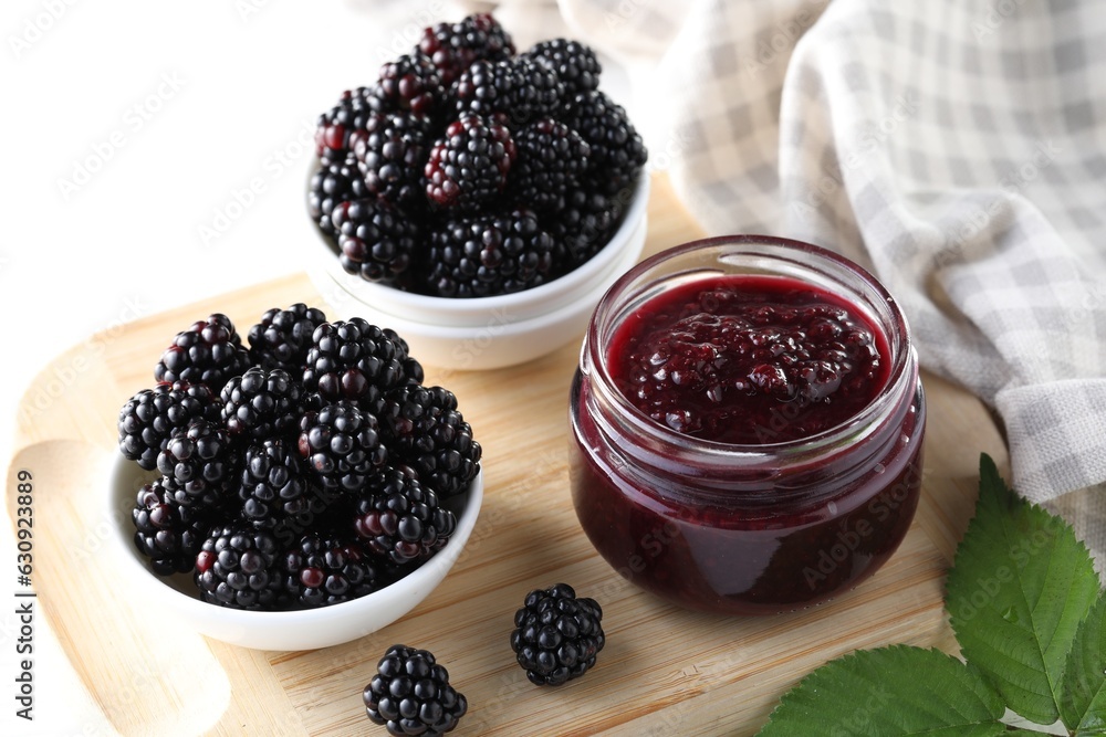 Fresh ripe blackberries, tasty jam and leaves on wooden board, closeup Fresh ripe blackberries, tasty jam and leaves on wooden board, closeup
