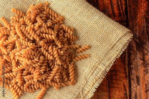 Raw whole grain fusilli pasta on rustic fabric over wooden table. photo