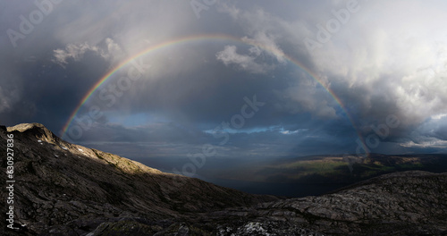 Wide angle panorama of a Rainbow over a Norwegian valley and mountains. Dramatic light rainbow storm. High contrast scenery Norway. Regnbåge Smaltinden, Luröy, Helgeland, Norge. Mountain storm light.  photo