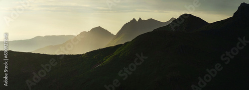 Panorama of abstract norwegian landscape at sunset, Smaltinden, Luröy, Helgeland, Nordnorge. Post summer storm dusk with mountain silhouettes. Green details in dark mountains scandinavia. Sommarnatt