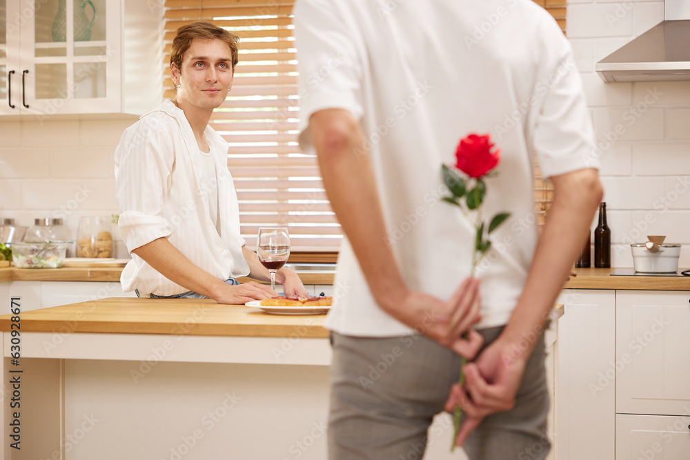 young gay couple looking at boyfriend and holding rose behind his back for surprise in the kitchen