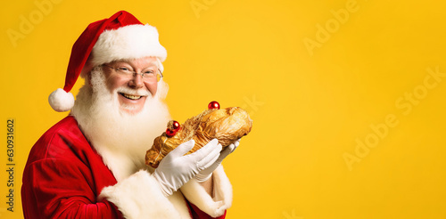 Santa Claus with Santa Claus suit and hat, smiling at the camera with a turkey or bread in his hands. Isolated on a yellow background