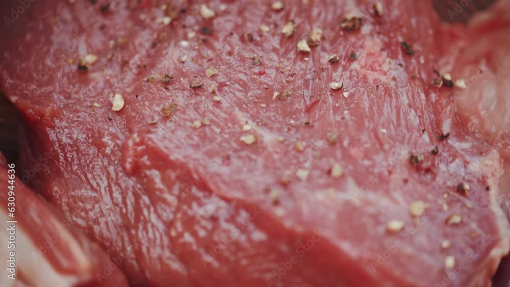Fresh appetizing raw steak is seasoned with salt and pepper close up before cooking on a barbecue grill. Concept of cheerful outdoor BBQ party Fresh appetizing raw steak is seasoned with salt and pepper close up before cooking on a barbecue grill. Concept of cheerful outdoor BBQ party