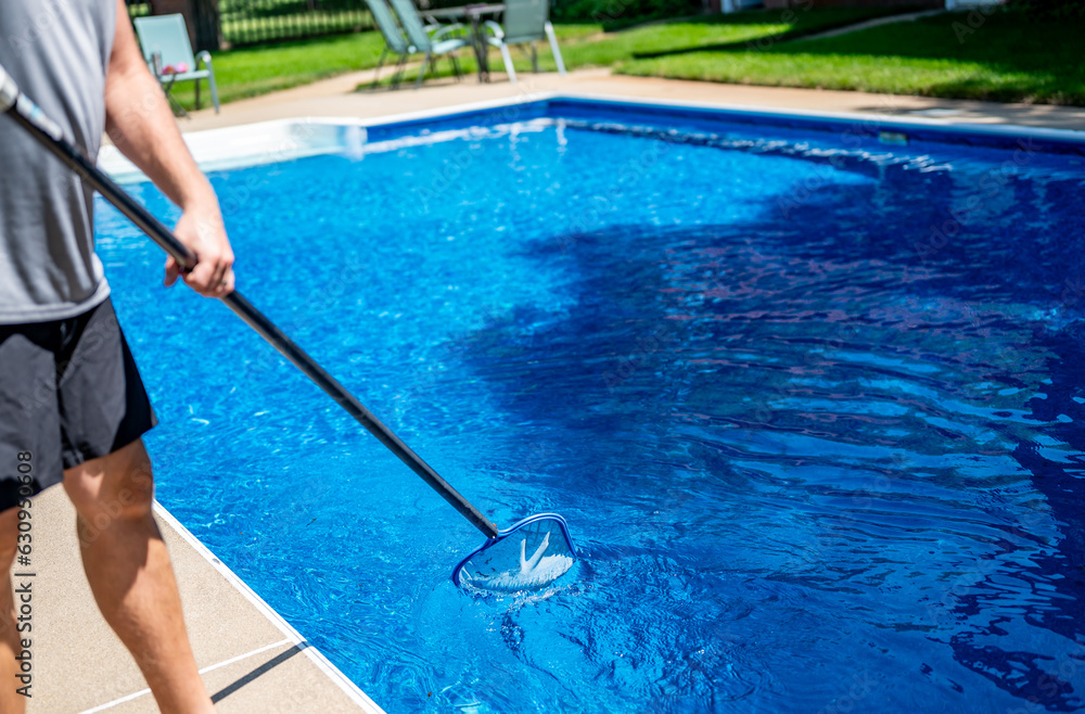 Boy using a skimmer to collect leaves out of a swimming pool