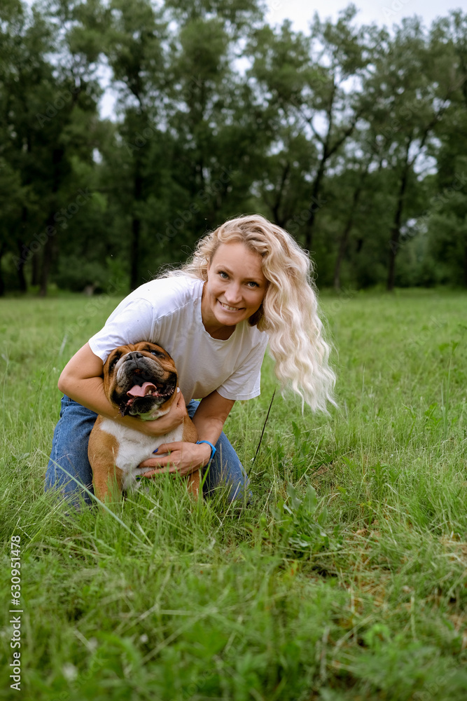 young blond woman laying with English Bulldog on meadow at park. Portrait close up