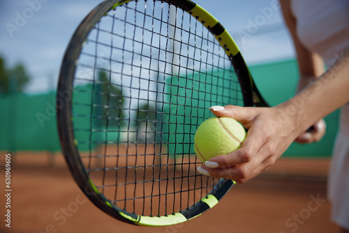 Closeup selective focus on ball and tennis racket in female hand