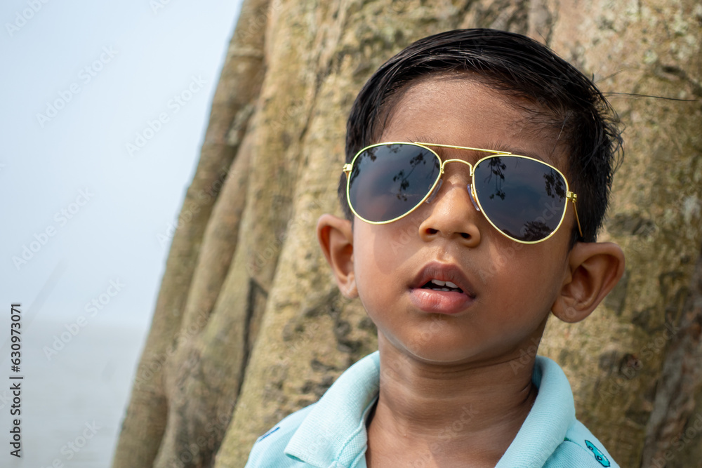 Sunglass wearing an Asian kid’s closeup portrait. Moody Asian boy looking at the camera.