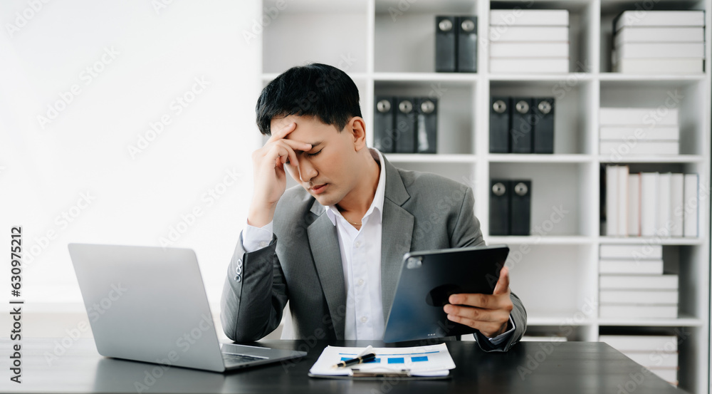 Frustrated young businessman working on a laptop computer sitting at his working place in office Frustrated young businessman working on a laptop computer sitting at his working place in office