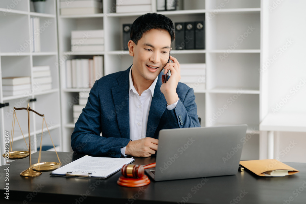 Asian male lawyer chatting online with client on laptop, smartphone discussing details of lawsuit. in office Asian male lawyer chatting online with client on laptop, smartphone discussing details of lawsuit. in office