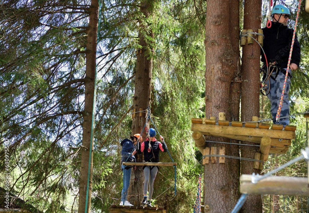 Man and a woman climb the wooden stairs at a height in amusement rope park